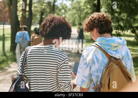 Diverse Teen Students Using Smartphone while Walking on Campus Path Stock Photo