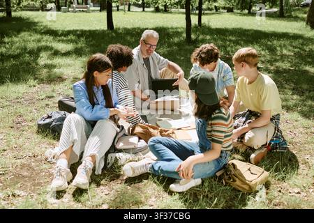 Diverse Teen Students Studying Outdoors with Teacher Using Laptop Stock Photo