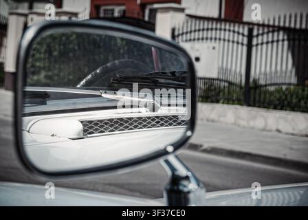 Macro close-up of a chrome vintage car side mirror reflecting the windshield wiper and cowl vent of a classic Hillman automobile on a street Stock Photo