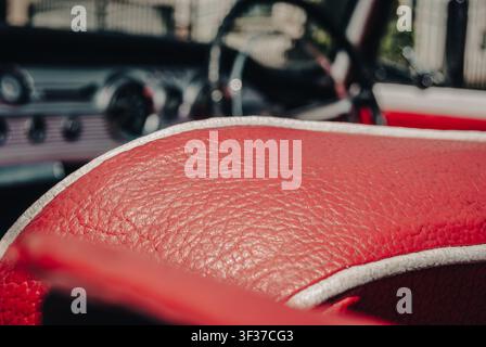 Macro close-up of red textured leather interior upholstery and white piping in a classic vintage car, with a blurred dashboard in the background Stock Photo