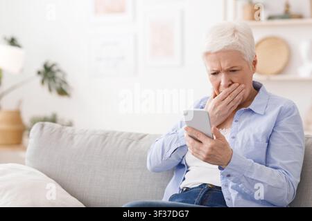 Worried senior lady reading shocking news on smartphone at home Stock Photo