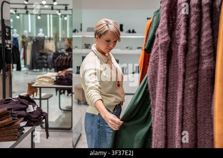 Woman shopping for clothes in store. Customer choosing wool sweater from rack. Fashion boutique interior with apparel collection. Retail lifestyle Stock Photo