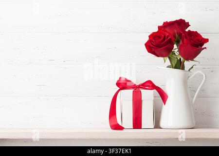 Valentines day greeting card with rose flowers bouquet and gift box in front of wooden wall with space for your greetings Stock Photo