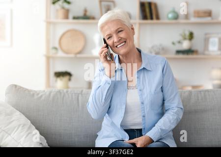 Communication Concept. Smiling elderly woman talking on mobile phone at home Stock Photo