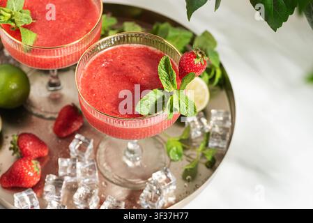 Two glasses of refreshing strawberry margarita cocktails garnished with fresh mint leaves, lime slices, and whole strawberries on a silver tray with s Stock Photo