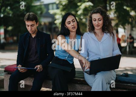 Business colleagues collaborating outdoors with laptop and clipboard on a park bench Stock Photo