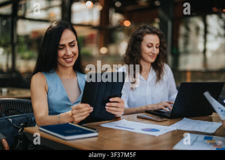 Two women working together on tablet and laptop in casual business meeting at cafe Stock Photo