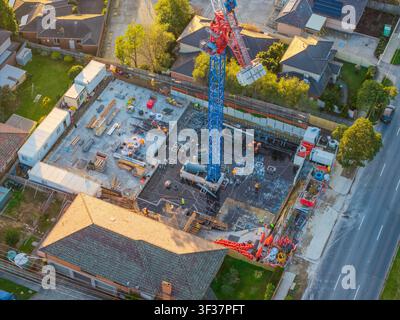 Aerial view of an active suburban construction site featuring a tall crane and workers during golden hour, highlighting urban growth and development. Stock Photo