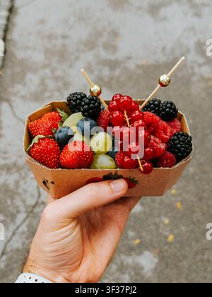 Close-up of a hand holding a cardboard tray filled with fresh berries and grapes purchased at the Central Market in Ljubljana, Slovenia. Stock Photo