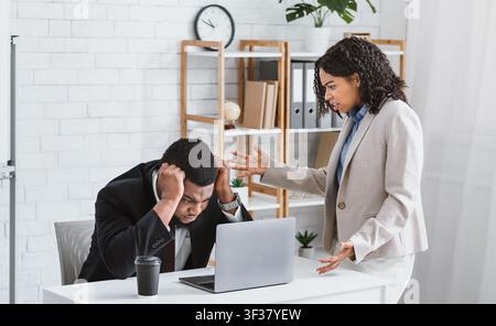 Frustrated African American boss scolding young subordinate for making mistake in business project at office Stock Photo