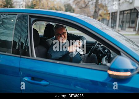 Smiling middle-aged man in blue car leaning out of the window holding a small plastic bag Stock Photo