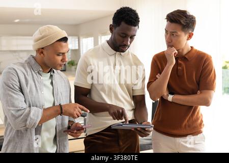 Diverse male coworkers in casual workwear pointing and discussing tablet in kitchen with smartphone Stock Photo