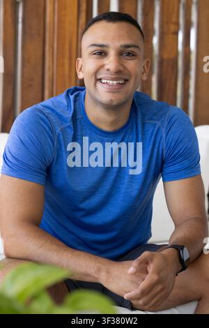 African American man sitting on white bench smiling, leaning wearing blue tee and watch near plant Stock Photo