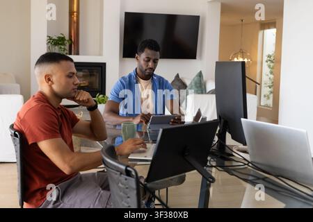 African American coworkers working at glass table at home in casual shirts using laptops and tablet Stock Photo