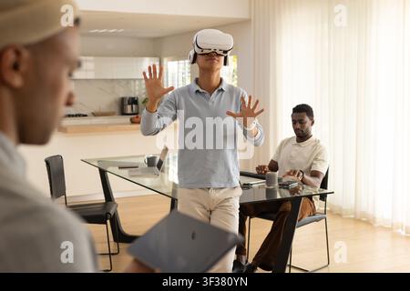 Diverse male coworkers testing virtual reality headset, using laptop and tablet at home dining area Stock Photo