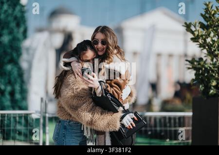 Two friends hugging and taking a selfie outdoors in winter coats, smiling and having fun Stock Photo