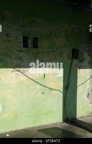 Abstract architectural composition featuring a weathered green wall illuminated by natural sunlight with dramatic shadows and minimalist geometric ele Stock Photo