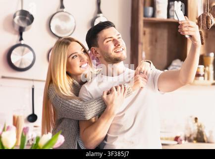 Happy Young Couple Taking Selfie In Kitchen, Smiling And Embracing, Love Concept Stock Photo