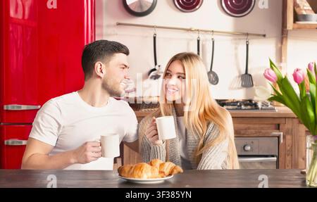Couple Enjoying Morning Coffee Together In Bright Modern Kitchen, Smiling And Relaxed Stock Photo