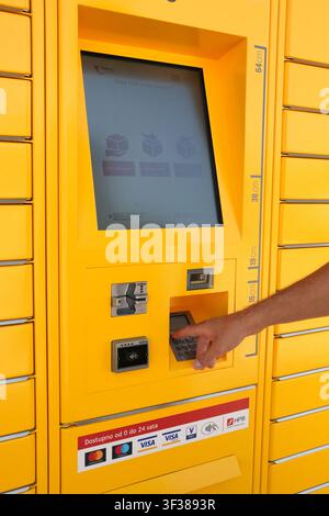 A man using the touchscreen interface of a yellow Paket24 parcel locker terminal, with options to pick up or send a package, in Rijeka. Stock Photo