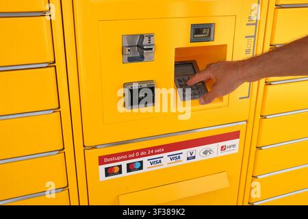 A detailed close-up showing a hand pressing buttons on the secure PIN keypad of a yellow Paket24 parcel delivery station. Stock Photo