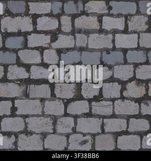 Top down view of traditional grey granite cobblestone pavement with dark dirt filled joints. Stock Photo