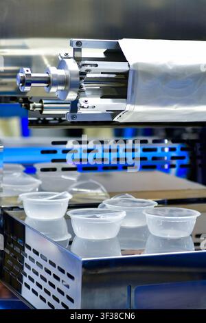 Automatic plastic tray sealing and packaging machine operating in food industrial factory Stock Photo