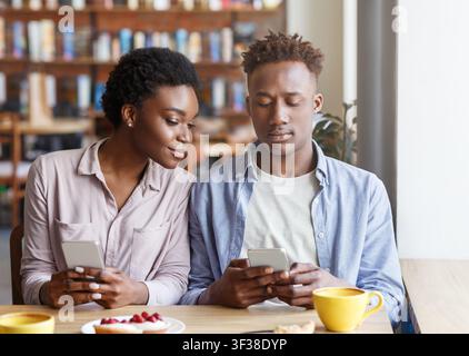 Couple Using Smartphones Together In Modern Cafe, Casual And Relaxed Atmosphere Stock Photo