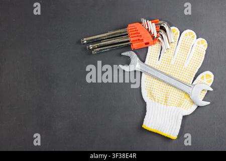 A set of hex keys, a metal spanner wrench, and a white work glove arranged on a dark surface with copy space on the left. High Quality Photo Stock Photo
