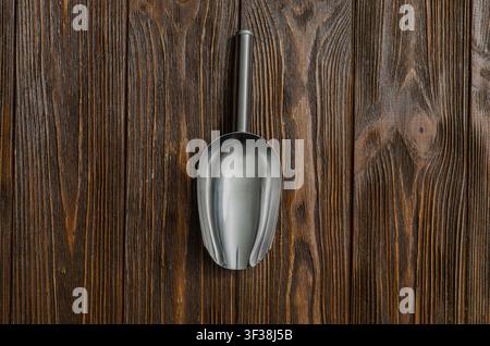 Top view of a stainless steel metal scoop placed on a rustic dark wooden surface with generous copy space. Stock Photo