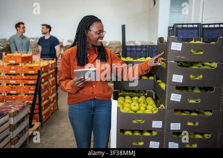 Female worker checking apple inventory in warehouse with tablet Stock Photo