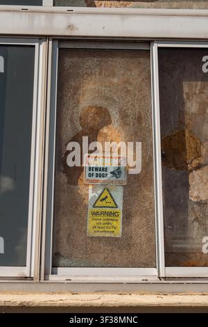 Seven Sisters, Hastings – 2026.03.28 – Broken window with 'Beware of Dogs' and CCTV warning signs on a boarded-up premises. Stock Photo