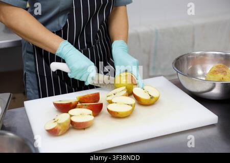 Woman in protective gloves slicing fresh apples on cutting board Stock Photo