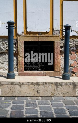 Architectural detail of a historic stone building basement window with wrought iron grate and metal bollards in Szentendre, Hungary. Stock Photo