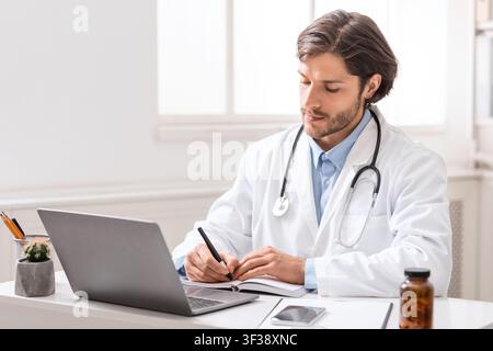 Focused watching webinar on laptop and taking notes at office Stock Photo