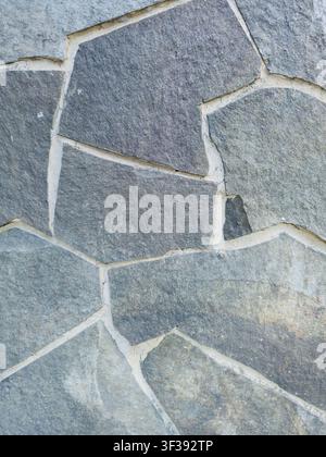 Close-up of a modern grey slate flagstone wall with clean white mortar joints and irregular geometric shapes. Stock Photo