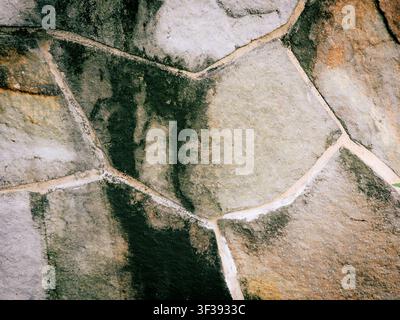 Close-up of a weathered stone wall featuring irregular flagstones, white mortar joints, and dark damp stains or mold growth. Stock Photo