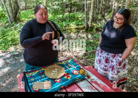 A cultural facilitator shows a participant the playing pieces for the traditional Mi’kmaq dice game, Waltes, at a picnic table on the Goat Island Trail in the Eskasoni First Nation, Nova Scotia, Canada. In the game, six discs, painted on both sides, are thrown from a wooden bowl and the points are counted using sticks Stock Photo