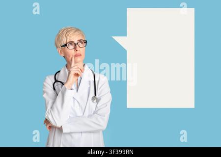 Female doctor in glasses and white coat presses her finger to chin and looks up at empty space Stock Photo