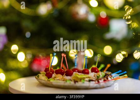 A closeup shot of various colorful appetizers on a plate, set against a festive, blurred background of Christmas tree lights Stock Photo