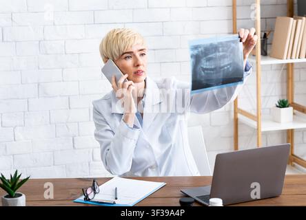 Female doctor talking on phone looking at x-ray of jaw Stock Photo