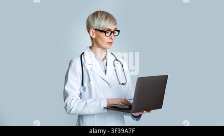 Modern doctor appointment concept. Woman doctor in white coat and glasses writing medical history to laptop Stock Photo