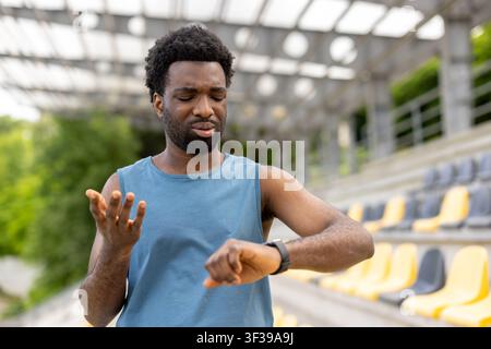 Athletic man feeling disappointed and frustrated, checking fitness tracker data after a workout or run in a stadium, reflecting on performance and setting new personal goals Stock Photo