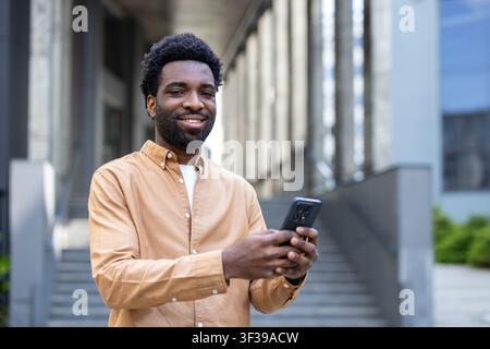 Smiling young person holding a mobile phone, connecting and communicating outdoors in an urban environment, representing modern technology and digital lifestyle Stock Photo