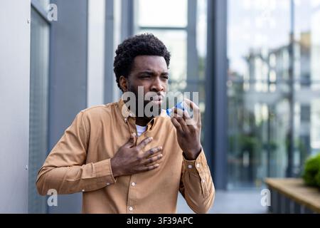 Young man experiencing an asthma attack and difficulty breathing, using an inhaler to alleviate chest pain and respiratory distress in an urban outdoor setting Stock Photo