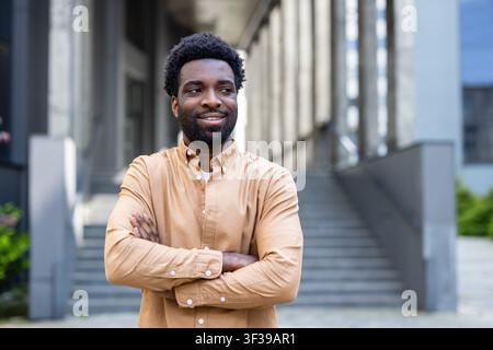 Young smiling african person standing confidently outdoors with arms crossed, looking away and expressing optimism for the future or success in an urban setting Stock Photo