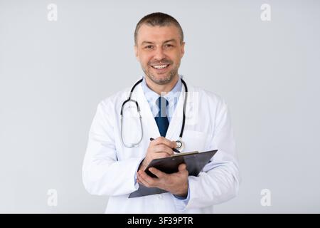 Portrait of mature doctor writing something on clipboard Stock Photo