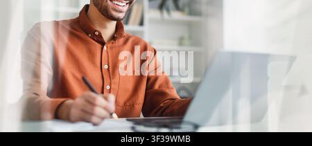 Smiling Young Caucasian Man Working On Laptop At Home Office, Business Concept Stock Photo