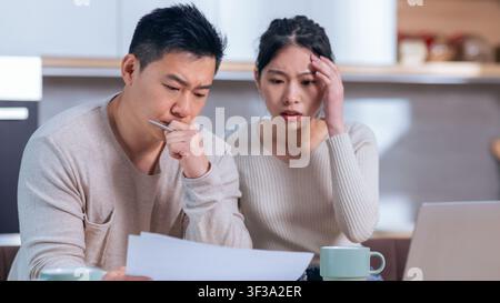 Worried Asian Couple Reviewing Financial Documents At Home, Business Concept Stock Photo