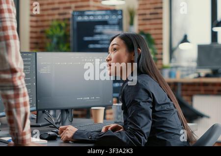 Database developer points a pencil at a computer screen while explaining a compiling algorithm to a coworker during a software team project. Stock Photo